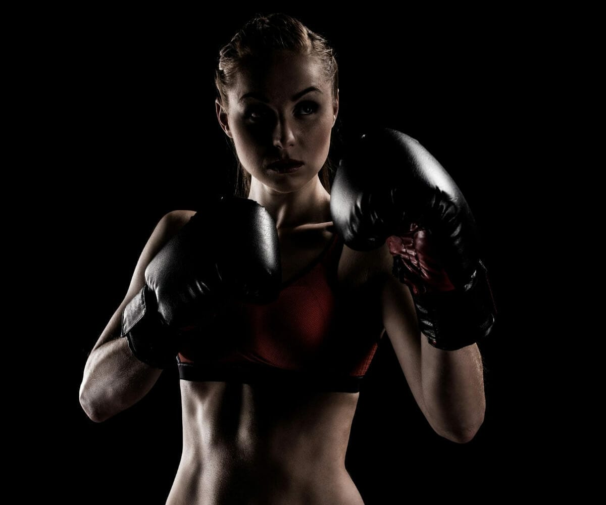 A woman posing on a black background, wearing boxing gloves.